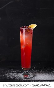 Cranberry Cocktail With Lemon And Ice Decorated With Powdered Sugar On Black Background Side View