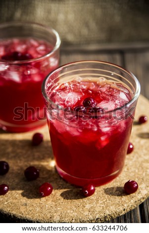 Cranberry mors with ice and berries. On a wooden table and a round cork stand