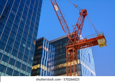 The crane against modern buildings under construction at dusk.