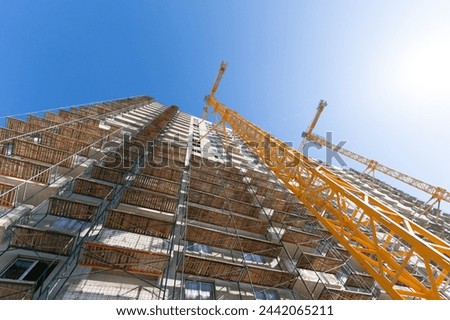 Crane and building under construction against blue sky. Construction work site. Construction of a multi-storey building using a high-rise yellow crane. Home construction.