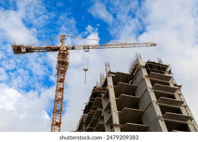 A crane in front of a building under construction. The sky is clear and blue. construction of a multi-storey building - Powered by Shutterstock