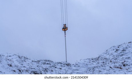 A Crane Hook On A Construction Site In Winter. The Boom Of The Tower Crane In Front Of The Snow-covered Hill Of The Earth. Industry Concepts.
