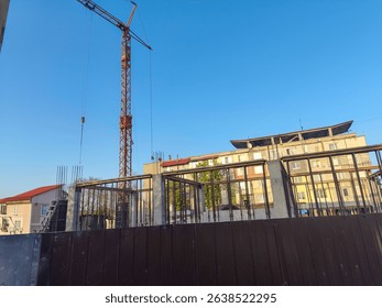 A crane is lifting a large object in front of a building. The sky is clear and blue