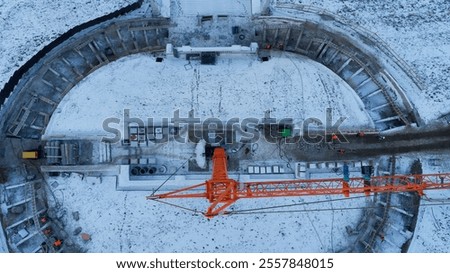 Crane is lifting a large object in the snow. The crane is orange and the object is white. The scene is cold and snowy, with the crane and the object standing out against the white background
