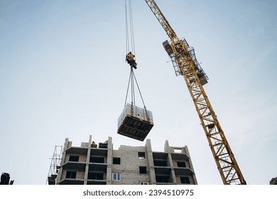 A crane lifts bricks to a height for the construction of a high-rise building. photograph of a construction site against a blue sky - Powered by Shutterstock