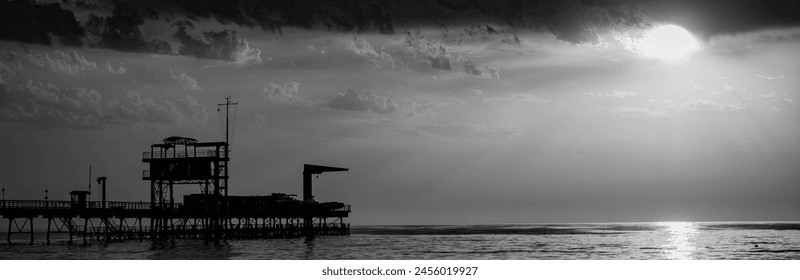 Crane on the sea pier in the rays of the setting sun. Silhouette of a pier on the sea horizon. Evening at sea on a cloudy day - Powered by Shutterstock