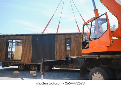 Crane operator lifting prefabricated modular house onto truck, showcasing efficient construction and transportation methods