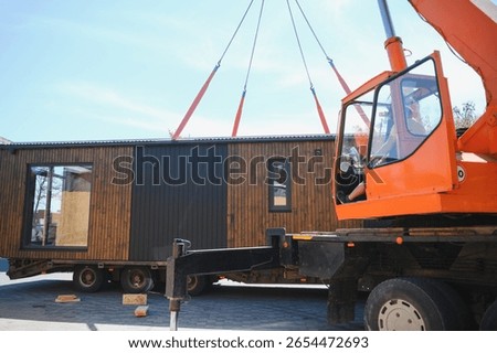 Crane operator lifting prefabricated modular house onto truck, showcasing efficient construction and transportation methods