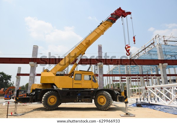 Crane operator and Mobile crane machine stand by\
waiting for lift steel roof truss under the construction building\
industrial factory