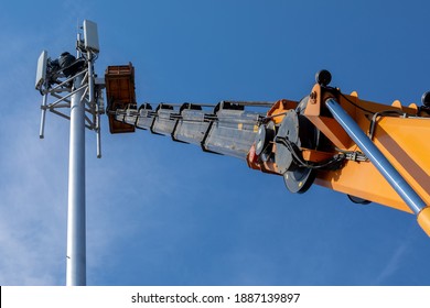 Crane With Telescopic Boom Lift Used As An Aerial Working Platform. Worker Install Cellular Base Station With Transmitters 3G, 4G And Antennas On Cell Tower On Background Of Blue Sky. Focus On Arrow.