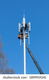 Crane With Telescopic Boom Lift Used As An Aerial Working Platform. Worker Install Cellular Base Station With Transmitters 3G, 4G, And Antennas On Cell Tower On Blue Sky Background. Vertical