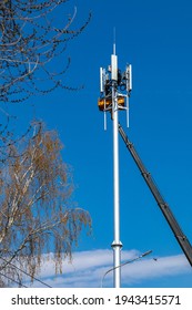 Crane With Telescopic Boom Lift Used As An Aerial Working Platform. Worker Install Cellular Base Station With Transmitters 3G, 4G, And Antennas On Cell Tower On Blue Sky Background. Vertical