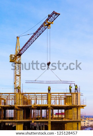 Crane and workers at  construction site against blue sky.