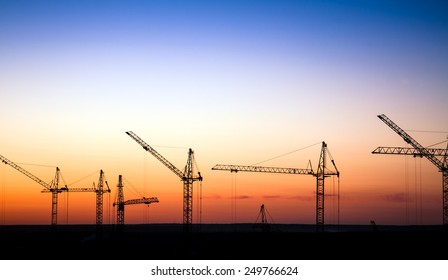 Cranes on a construction site against sunset sky