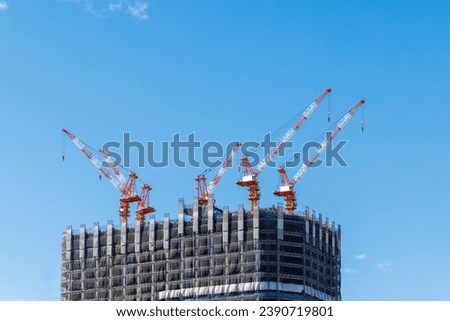 Cranes painted red and white operates on the roof of a building under construction