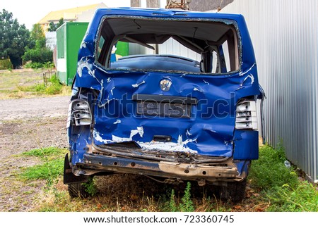 The crash car back view, broken minibus after accident. Failed blue van on country road, near a metal gray fence.