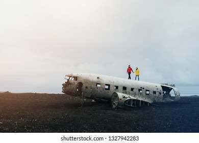 Crash Plane In Iceland. Two Travelers In Red And Yellow Jacket.