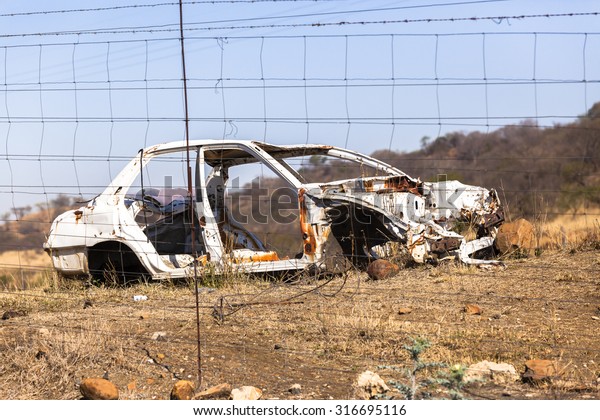 Crashed Car \
Crashed Car wreck\
destroyed stripped vehicle body behind electrical\
fence