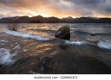 Crashing waves on lake shoreline with dramatic sunset sky above mountains at Derwentwater in the Lake District, UK. - Powered by Shutterstock