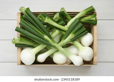 Crate with green spring onions on white wooden table, top view