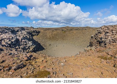 Crater of a volcano in the day with sunshine and clouds in the sky. Landscape on Iceland of Reykjanes Peninsula. Brown and gray lava rocks and along the rim of the crater