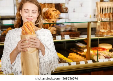 Craving for the first bite. Half length portrait of a pretty cheerful female smelling fresh bread smiling happily 