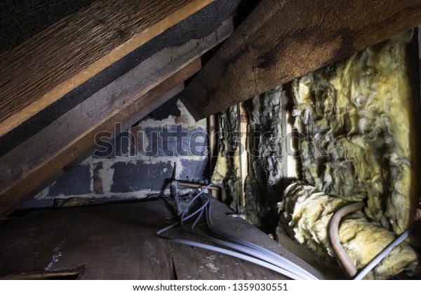 Crawl space under the eves of a house showing\
old fibreglass insulation, pipework, rafters, breezeblock\
construction and old\
boarding.