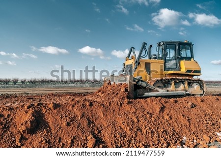 Crawler bulldozer working on construction site or quarry. Mining machinery moving clay, smoothing gravel surface for new road. Earthmoving, excavations, digging on soils.