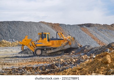 Crawler dozer working on construction site or quarry. Mining machinery moving clay, smoothing gravel surface for new road. Earthmoving, excavations, digging on soils