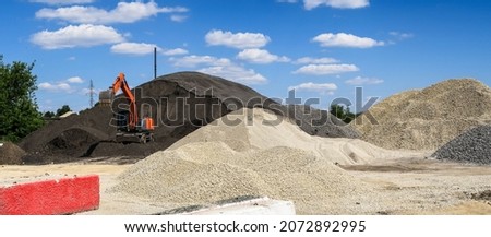 a crawler excavator loads crushed stone and sand into a truck. Large hills and piles of sand, gravel, crushed stone of white, gray and black color.                       