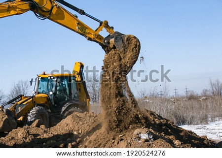 Crawler excavator. The excavator in the process of work digs out the earth and pours it onto the site. Works on a clear winter day against the blue sky.