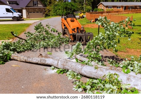 Crawler tractor loader machine removes large tree debris from road in quiet neighborhood following recent bad weather.