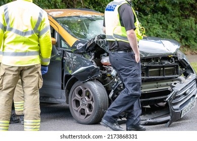 CRAWLEY WEST SUSSEX UK - JUL 02 2022: RTC Police Man Walking In Front Of A Smashed Car With Firemen