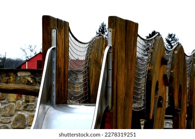 crawling wooden attraction on the sandpit. children have a stainless steel slide and rope nets for climbing and for greater safety on the bridge. stone sandstone wall in the background of kindergarten - Shutterstock ID 2278319251