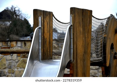 crawling wooden attraction on the sandpit. children have a stainless steel slide and rope nets for climbing and for greater safety on the bridge. stone sandstone wall in the background of kindergarten - Shutterstock ID 2278319359