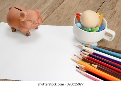 Crayons And Piggy Bank On A Sheet Of Paper