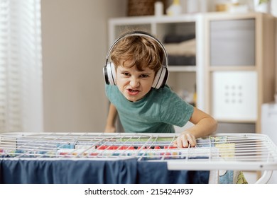 A crazed happy young boy fools around while doing household chores. The child has wireless headphones listens to music, plays DJ using a clothes dryer.
