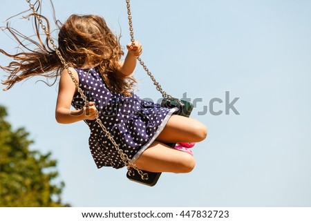 Craziness and freedom. Young summer girl playing on swing-set outdoor. Crazy playful child swinging very high to touch the sky.