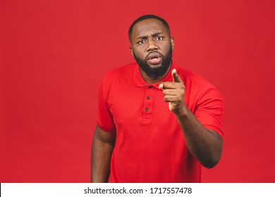Crazy angry African American man pointing finger, looking at camera, mad young male quarreling, blaming anybody, shouting, feeling aggression, conflict concept, isolated over red background.