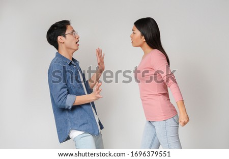 Crazy angry asian girl wants to punch his boyfriend, grey studio background