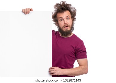 Crazy Bearded Man With Funny Haircut Showing Empty Blank Signboard With Copy Space. Guy With Surprised Eyes And Mouth Open Peeking Out From Behind Big White Banner, Isolated On White Background.