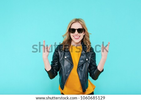 Crazy beautiful rock Girl in leather jacket and black sunglasses. Punk is not dead. Attractive cool young woman making horn sign hand gesture.