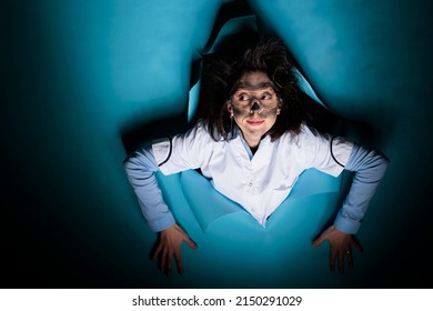 Crazy Biochemistry Expert With Goofy Face Expression And Wacky Look Acting Funny While On Blue Background. Lunatic Chemist With Messy Hair An Dirty Face Looking At Camera. Studio Shot.