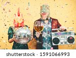Crazy couple celebrating new year eve wearing chicken and dinosaur t-rex mask - Young trendy people having fun drinking champagne and listening music with vintage boombox - Absurd and holidays concept