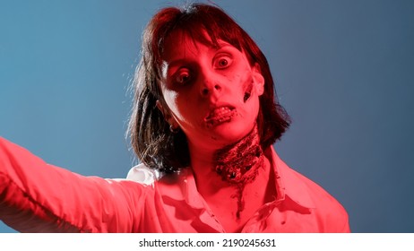 Crazy Dangerous Brain-eating Zombie Surrounded By Police On Blue Background. Creepy Looking Mindless Walking Dead Corpse With Deep And Bloody Wounds And Scars Growling At Camera. Studio Shot