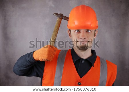 Crazy desperate worker with a funny expression hits himself on the head with a hammer