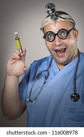 Crazy Doctor With A Syringe And Goofy Glasses. Young Man Smiling And Holding Syringe With Yellow Medicine