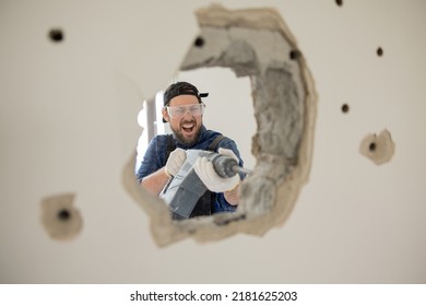 Crazy energetic man vandalizes apartment with impact hammer forges wall punches a hole through concrete, house construction site.