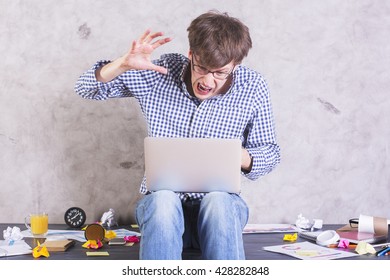 Crazy Frastrated Businessman Sitting On Messy Office Desktop About To Hit His Laptop With Hand