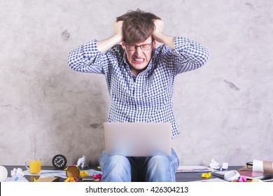 Crazy Frustrated Businessman With Laptop Sitting On Messy Office Desktop And Pulling His Own Hair